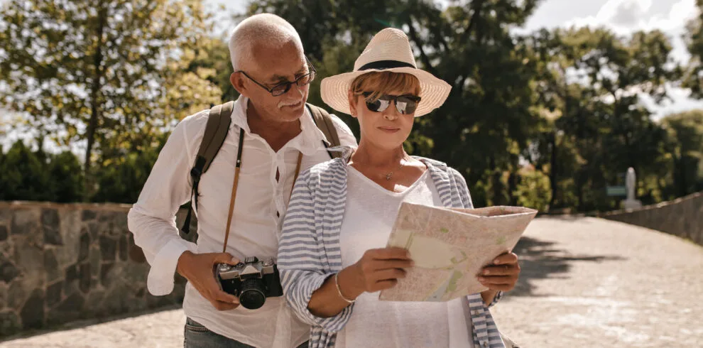 Modern woman in white t-shirt, striped blouse, hat and glasses looking at map and walking with grey